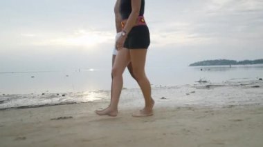 Side view - interracial couple walking on an exotic island beach along the sea at sunset matching leg steps - unrecognizable - 4K Horizontal video