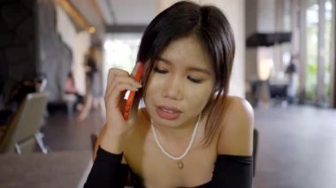 Slider shot of Beautiful young Asian woman who talks on the telephone sitting on a sofa in a lounge of a hotel. - 4K horizontal video