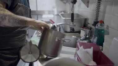 Erkek aşçının mutfakta muslukla su doldurduğu yan manzara - 4K Yatay video