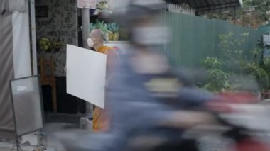 Adult Thai monk walking at Bangkok street with blank poster wearing face mask - 4K Horizontal video