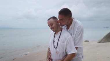 Embraced gay couple in 30th walking along tropical beach and kissing during summer vacation - 4K Horizontal video