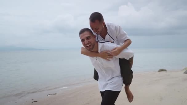 Cheerful Gay Man Giving Piggyback Ride His Partner Beach Horizontal — Wideo stockowe