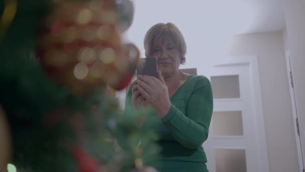 Жінка Пенсіонер Будинку Захоплююча Фотографія Блискучої Різдвяної Ялинки Камерою Мобільного — стокове відео