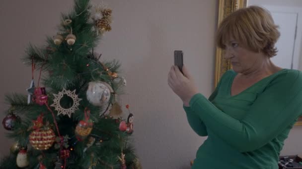 年迈的寡妇在建造圣诞树后拿着手机在圣诞树上拍照 中镜头 水平4K视频 — 图库视频影像