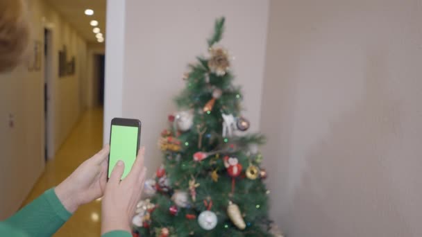 房子里的女人用智能手机相机给装饰圣诞树拍照 选择性焦点 水平4K视频 — 图库视频影像