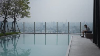 Adam Tayland 'da Bangkok' ta bir binanın havuz başındaki bir salonda dizüstü bilgisayar kullanıyor. Statik Çekim - 4K Yatay Görüntü