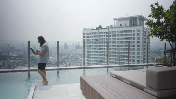 Long Haired Guy Holding Computer Laptop While Walking Rooftop Pool — 비디오
