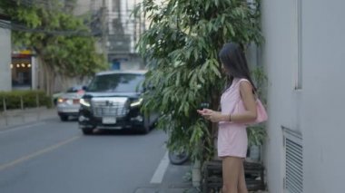 The girl is standing on the street playing a game on her phone and the camera is zooming towards her - 4K Horizontal video