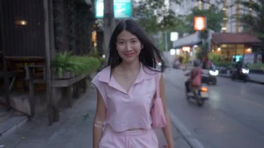 Cute girl walking happily on the street with headphones on her ear and a bag on her shoulder - 4K Horizontal video