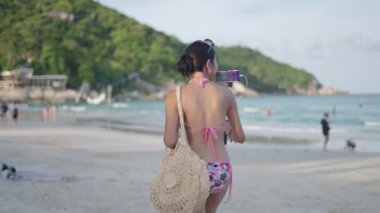 Taylandlı kız video blogcusunun Koh Phangan adasındaki bir plajda mayolu yürüyüşü - 4K yatay video