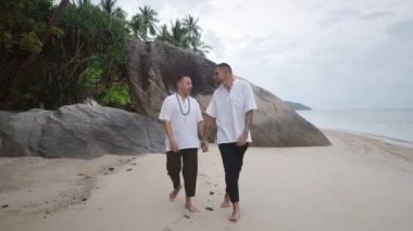 Lovely gay male partners walking along the tropical beach holding hands and chatting - 4K Horizontal video