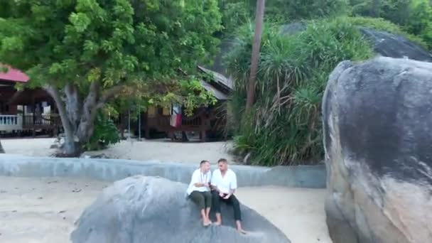 Reversing Aerial Shot Gay Couple Sitting Rock Talking Tropical Villa — Vídeo de Stock