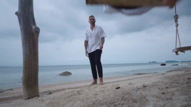 Married happy gay couple having fun on a beach seaside swing. Adult man push on his husband riding a swing on hazy day at tropical island - 4K Horizontal video
