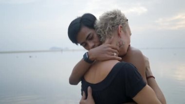 Bust shot of Thai young man and mature caucasian woman kissing at seaside sunset beach - slow motion - 4K Horizontal video