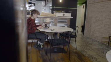 Short-haired woman drinks coffee and uses computer in empty restaurant - 4K Horizontal video
