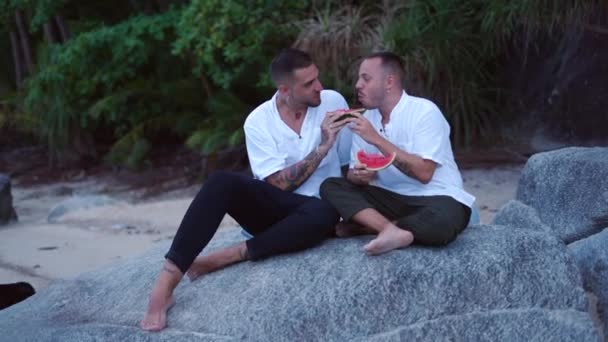 Happy Caucasian Gay Male Couple Eating Watermelon Sitting Rock Tropical — Video Stock