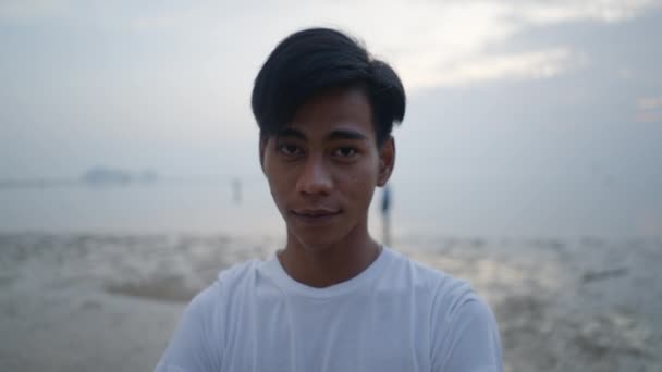 Молодий Тайський Чоловік Дивиться Камеру Посміхається Стоячи Біля Моря Заході — стокове відео