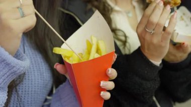 Two girls friends eating Valencia street market food at night - potato fries and chocolate waffle - face and hands closeup - 4K Horizontal video