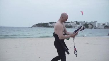 Masculine Man At The Beach Preparing Kite String For Kitesurfing In Mallorca, Spain. tracking shot - Horizontal