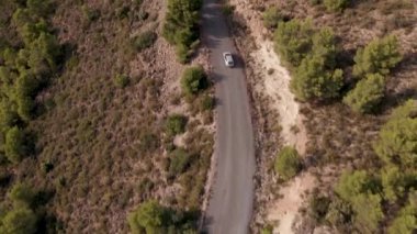 İki arabalı bir dağ yolu üzerinde 4K yatay video ile bir kasabanın eğik insansız hava aracı görüntüsü.