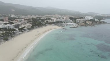 Clear And Turquoise Blue Water At Porto Novo Beach - Es Carregador Beach With Yacht Club On A Rainy Day In Mallorca, Spain. - aerial pullback - Horizontal