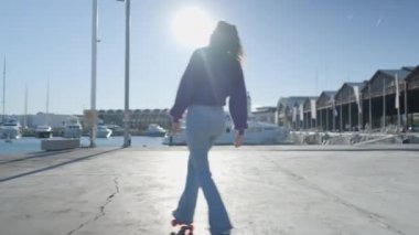 Girl roller skates by boats in harbor in sunlight, slomo from behind - 4K Horizontal video