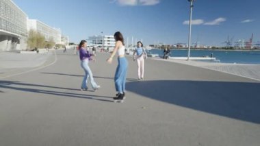 Üç kız, liman ve sirkte paten üzerinde dönüyor, güneş ışığı - 4K yatay video