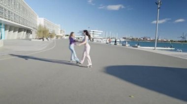 İki kız el ele tutuşup etrafında dönüyor ya da gün ışığında paten kayıyor - 4K Yatay Video