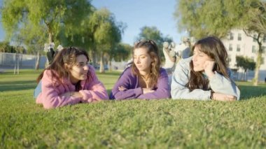 Girls with rollerskates lie on grass in sunlight and chat, ground view - 4K Horizontal video