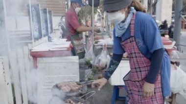 Kadın Satıcı Tayland, Bangkok 'taki sokak yiyecek dükkanında et pişiriyor. El bilgisayarı - 4K Yatay Görüntü
