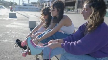 Slomo side view of three girls tying rollerskates on sunny windy day - 4K Horizontal video