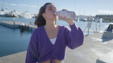 Close slomo of girl in purple top by harbor drinking out of bottle - 4K Horizontal video
