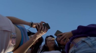 Young happy dark-haired women use phones and chat, seen from below - 4K Horizontal video