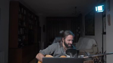 Young bearded songwriter performing a concert in his living room because of covid pandemic - Middle shot