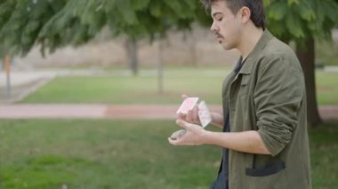 Erkek bir sokak sihirbazının gündüz vakti güzel bir bahçenin önünden geçerken kartlarla oynadığı yakın çekim. - 4K Yatay Görüntü