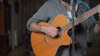 Caucasian young man singing and playing the guitar standing in his living room - Middle shot