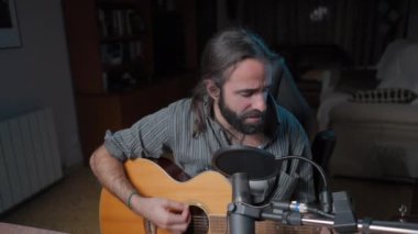 Musician playing guitar while smiling at his home studio - Middle shot