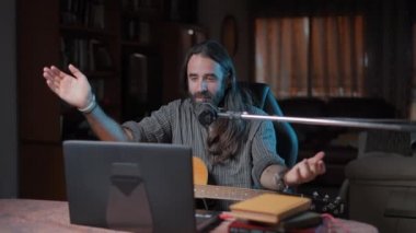 Genç sakallı müzisyen şarkılarından birini internetten dinleyicilerine çalıyor.