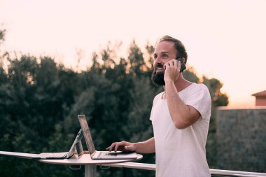 Genç bir girişimci orman evinde tabletiyle çalışırken telefon görüşmesi yapıyor. İş adamı konsepti.