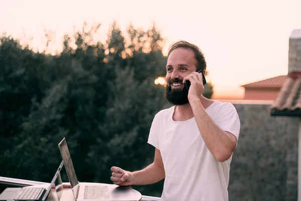 Genç bir girişimci orman evinde tabletiyle çalışırken telefon görüşmesi yapıyor. İş adamı konsepti.