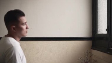 Handsome young latino approaches and looks out the window then gives a look at the camera. - Horizontal video