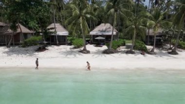 Bir çiftin beyaz kumda koşarken eğlendiği güzel bir sahilin havadan görünüşü. Turkuaz suyun güzel manzarası - 4K Yatay video