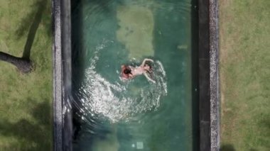 An aerial view from flying drone of a seductive sexy model in swimwear is enjoying with her partner in a pool during her summer weekend - 4K Horizontal video