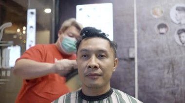 Bir erkek müşterinin kuaför tarafından 4K yatay kuaförde saçını kestirirken çekilmiş yakın plan bir fotoğrafı.