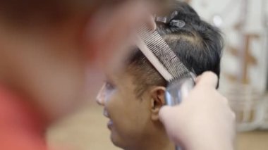 A static view of a smiling man sitting in a barber shop while professional barber making him a hair cut 4K Horizontal video