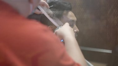 Bir berberin yan görüntüsü, havalı bir berber dükkanında çocukların saçlarını elektrikli makasla keser.