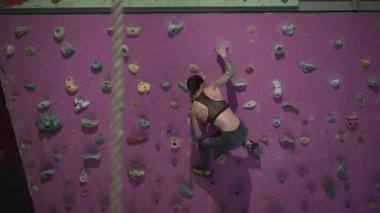 Fit girl climbing artificial rock wall with detail of climbing rope - Horizontal video