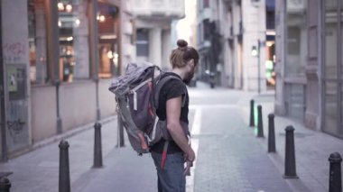 Young explorer lost in the city looks at the camera then turns his back and walks in the middle of the street - Horizonal video