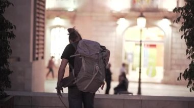 Young backpacker with dirty feet arrives at a wall and lays down while looking at his phone - Horizonal video