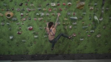 Fitness professional woman arrives at the artificial rock wall and starts climbing - Horizontal video